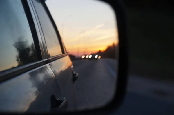 blurred road and sunset in car rearview mirror close up