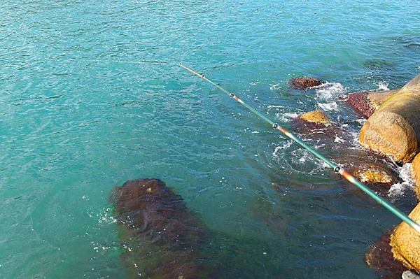 Spinnrute Zum Fischen Vor Dem Hintergrund Von Meerwasser Und Küstensteinen — Stockfoto