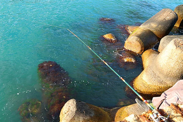 Spinnrute Zum Fischen Vor Dem Hintergrund Von Meerwasser Und Küstensteinen — Stockfoto