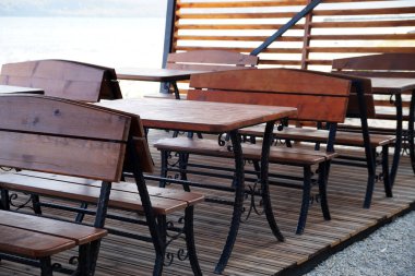 Boş ahşap masalar ve güneş ışığında bir sokak kafesinde banklar.