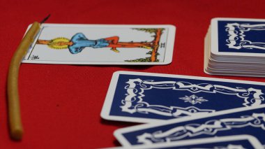 dağınık tarot kartlarından oluşan bir deste ve kırmızı arka planda bir mum..