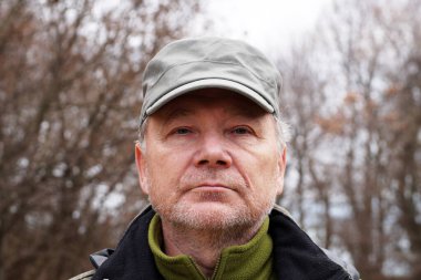 Doğanın arka planında şapkalı yaşlı bir adamın portresi..