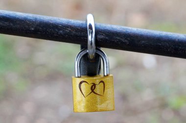 Korkulukta asılı iki kalp resmi olan sarı kilit.