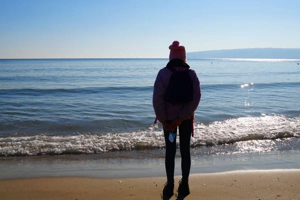 의료용 마스크를 소녀가 해변에 돌아보며 바다를 바라본다 — 스톡 사진