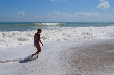 Genç kız güneşli bir günde boş deniz kıyısında tek başına yürüyor..