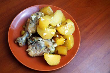 Tahta arka planda seramik tabakta tavuk ve sarımsaklı patates yahnisi..