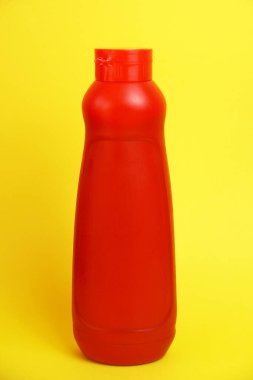 Sarı arka planda ketçaplı kırmızı plastik şişe.