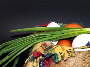 Beyaz ve kahverengi yumurtalar ve bir demet yeşil soğan kareli bir peçetenin üzerinde yakın plan siyah bir kasede.