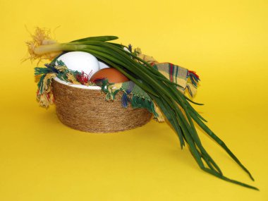 Beyaz ve kahverengi yumurtalar ve sarı arka plandaki bir kasede kareli bir peçete üzerinde bir demet yeşil soğan..