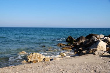 Boş kumlu sahil, sahilde büyük taşlar, deniz ufku ve açık gökyüzü..