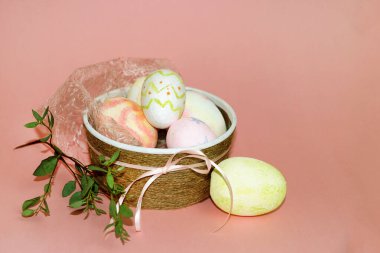 Boyanmış yumurtalarla dekoratif kase ve pembe arka planda mersin dalı, paskalya konsepti.