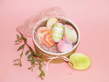 Paskalya konsepti, boyalı yumurtalarla dekoratif kase ve pembe arka planda bir mersin dalı.