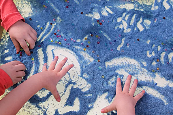 childrens hands touching blue sand on white table, sand therapy, development of fine motor skills