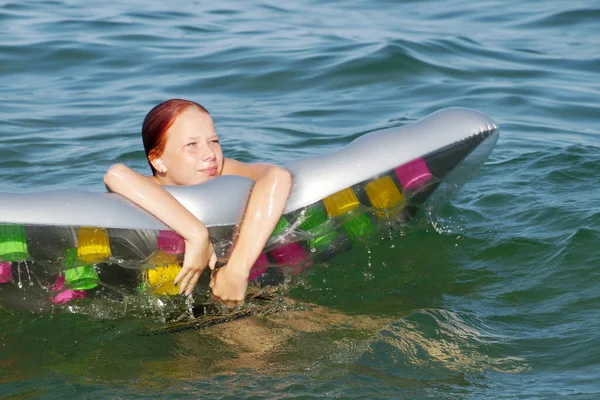 Suda şişme bir yatak tutan ve gülen genç bir kız..