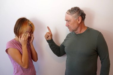 The father shakes his finger at his teenage daughter. The upset girl covered her face with her hands. Punishing children. clipart