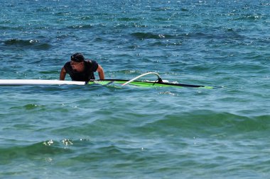 Rüzgâr sörfü tahtasının üzerinde duran bir adam suya düşen bir yelkeni kaldırır..