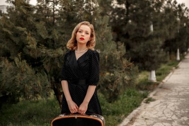 Siyah bir benekli elbise içinde, elinde eski bir valizle genç ve güzel bir kız..