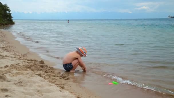 Niño pequeño está jugando en la playa en la arena, junto al mar — Vídeo de stock