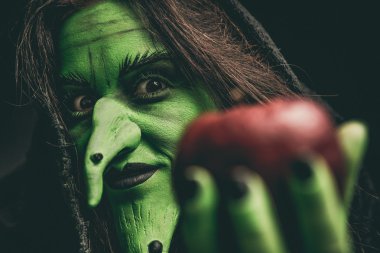 Evil witch looking at camera holding a red apple clipart