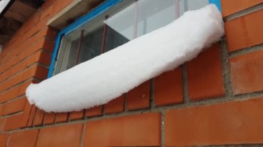 Pencerenin pervazında kar kapakları var. Kırmızı tuğlalı bir duvar ve parmaklıklı mavi pencere çerçevesi