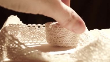 Kadın parmakları beyaz bir masada hassas bej dantele dokunur..