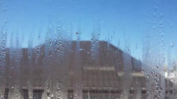 Close-up de uma janela fortemente embaçada. Céu e edifício com telhado de azulejos atrás de vidro — Vídeo de Stock