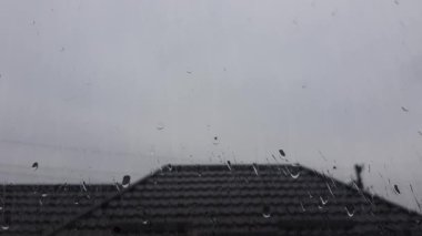 Yağmur damlalarındaki pencere. Cama su damlıyor. Çatı arka planda