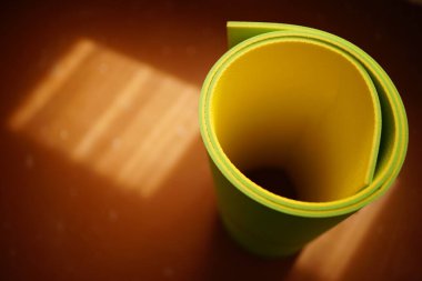 yeşil sarı yoga paspası güneşli zeminde yuvarlanıyor.