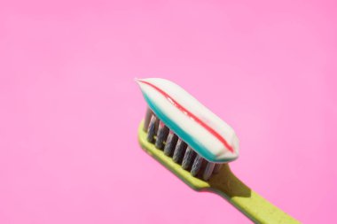 Pembe arka planda çizgili diş macunu olan yeşil plastik diş fırçası..