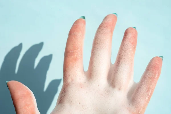 在蓝底蓝底的白色肥皂泡沫中 用阴影遮住女性的手指 — 图库照片