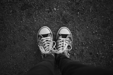 Spor ayakkabılı kadın ayağı ve asfalt yolda kot pantolon, üst manzara. BW fotoğrafı