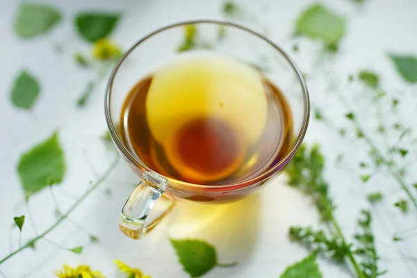 Зеленый Чай Стеклянной Чашке Зеленые Травы Цветы Белом Столе Вокруг — стоковое фото