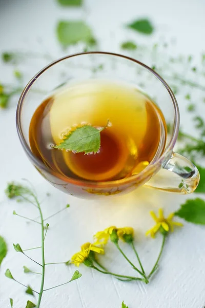 Green tea in a glass cup with herbs and flowers on a white table