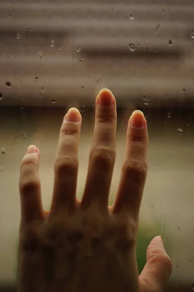 Hand touches a window in rain drops.