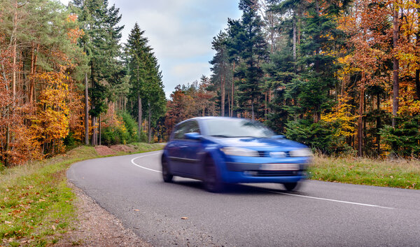 Speeding car blurred on arred road through colorful autumn trees