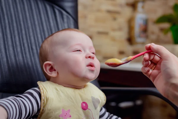 Bebê feliz na cadeira comendo mingau comida — Fotografia de Stock