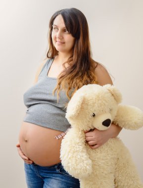 Hamile kadın beyaz bir oyuncak ayı tutarak durumda