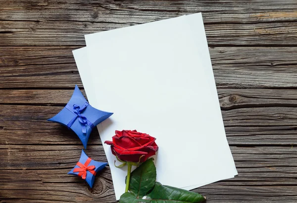 Papíry na stole s rudou růži a dárek — Stock fotografie