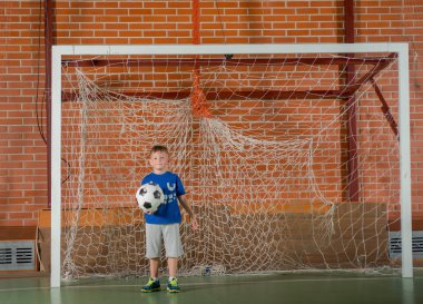 Bir futbol topu tutan kaleci oynayan genç çocuk