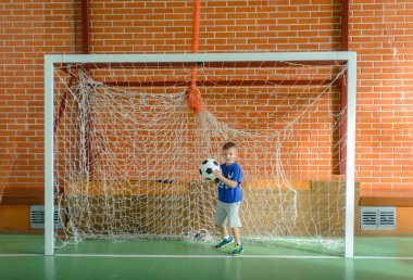 Bir futbol topu tutan kaleci oynayan genç çocuk