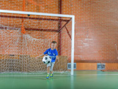 Bir futbol topu tutan kaleci oynayan genç çocuk