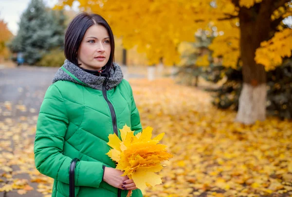 Beautiful young woman in green coat holding leaves — Stock Photo, Image