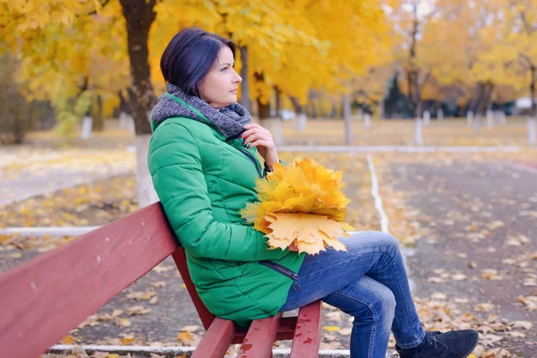 Pensive woman with large maple leaves on bench — Stock Photo, Image