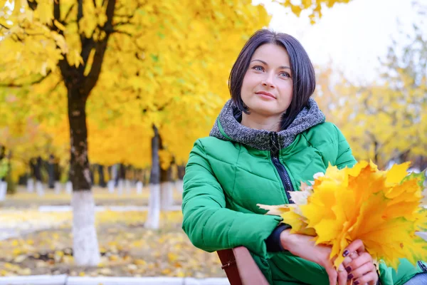 Nette Frau sitzt auf Bank neben gelben Bäumen — Stockfoto