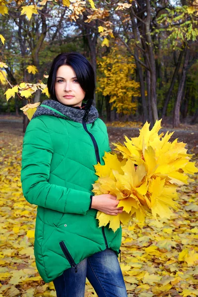 Serious woman looking at bundle of maple leaves — Stock Photo, Image