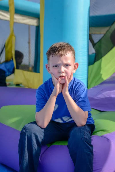 Pojke med svettiga ansikte sitter nära bouncy house — Stockfoto