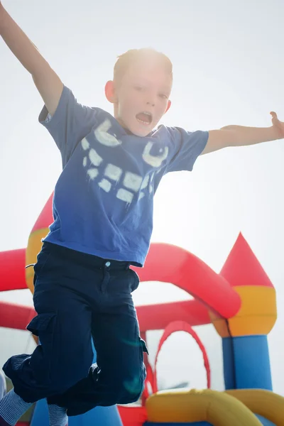 Opgewonden springen jongen in de buurt van springkasteel buitenshuis — Stockfoto