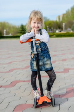 Bir scooter üzerinde poz gülümseyen küçük sarışın kız