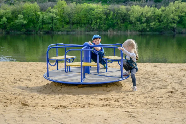 Dwoje dzieci roześmiany, grając na merry-go-round — Zdjęcie stockowe