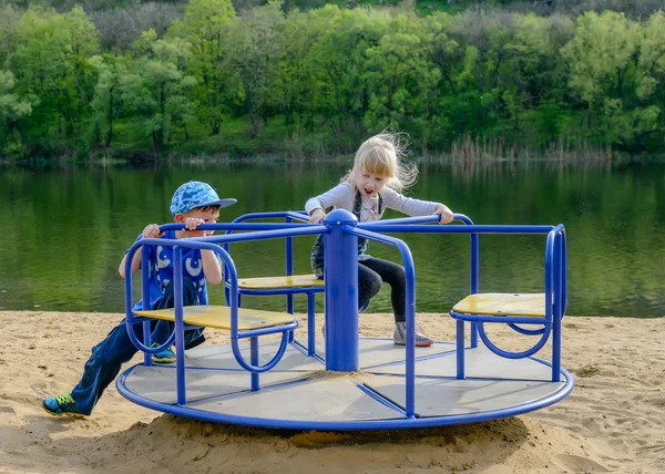 Dwóch młodych dzieci bawiące się na merry-go-round — Zdjęcie stockowe